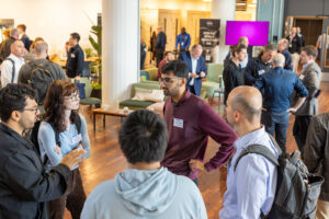 Attendees stand in small groups networking and talking in a bright conference venue during a professional event.